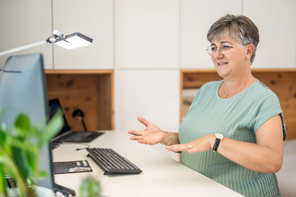 Eva Maria Hofstätter steht vor ihrem Schreibtisch und führt online eine Prana-Anwendung durch